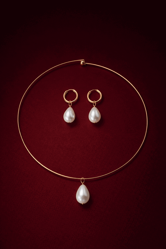 Gold cuff necklace with pearl pendants and a pair of gold hoop earrings with pearl pendants on a dark red background, Alba Duo Jewelry Set.