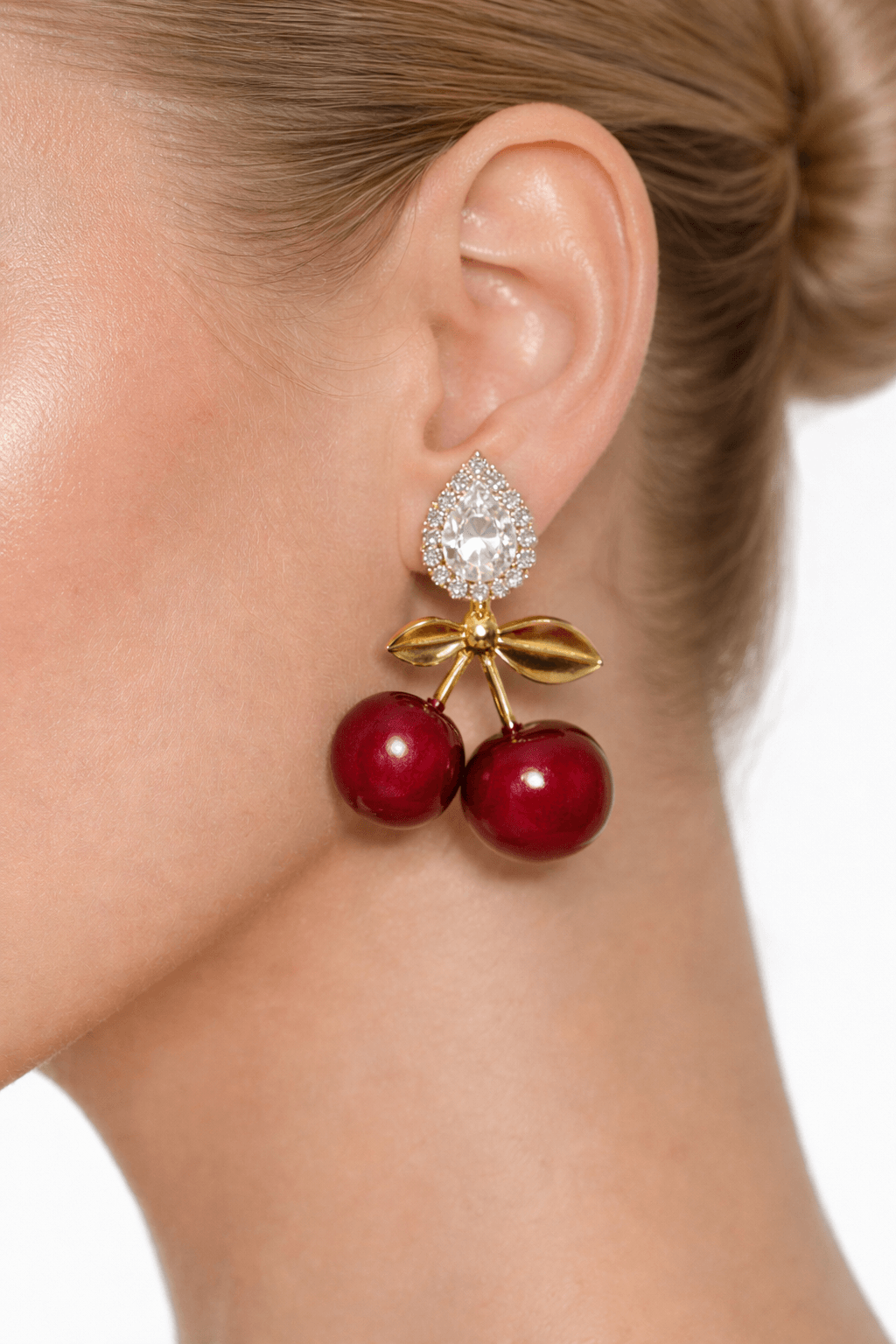 Close-up of an ear wearing a decorative earring with red cherries and a bow.