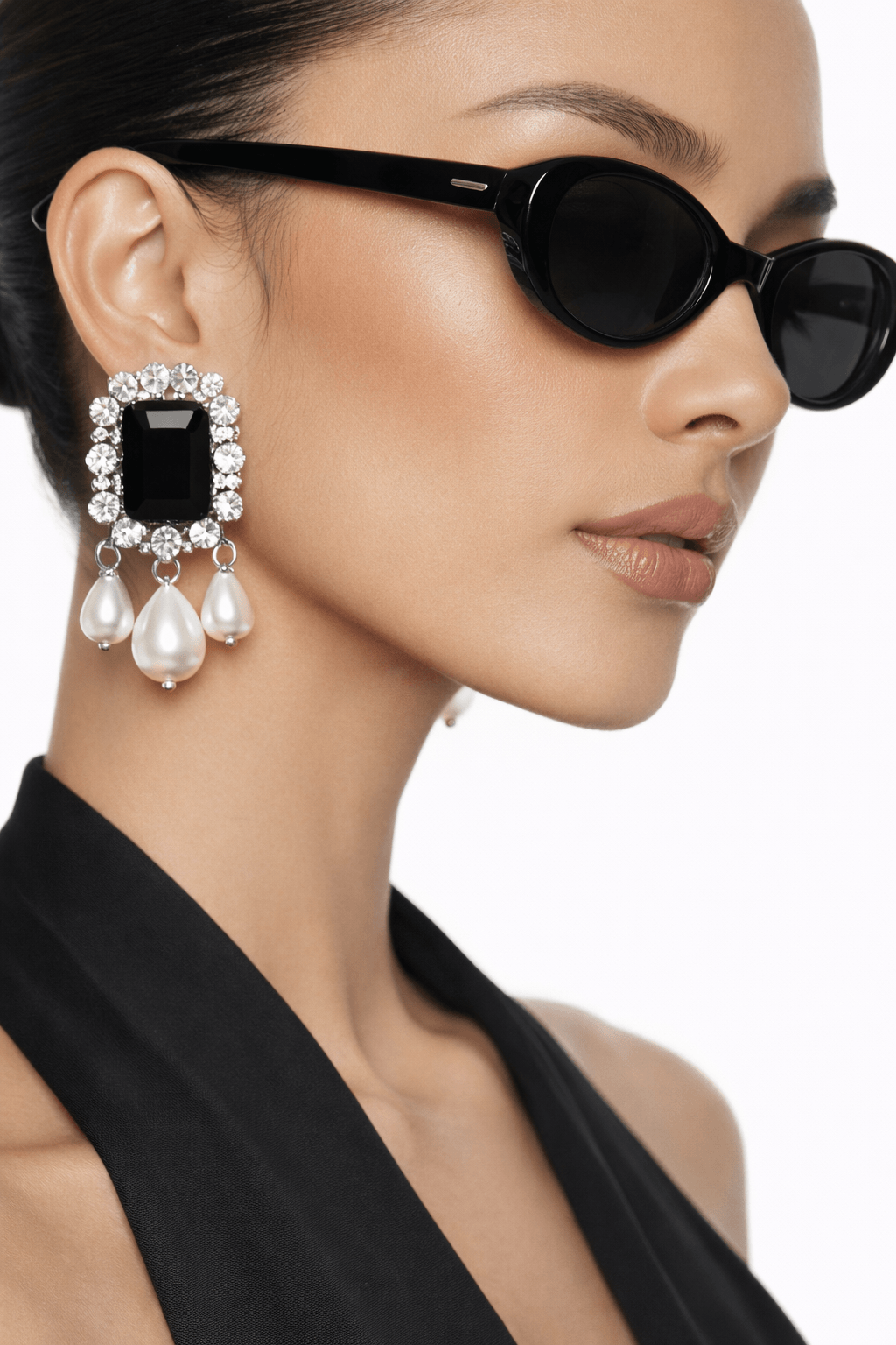 Close-up of a woman wearing statement black stoned earrings, black sunglasses and a black top with a focus on her earring.