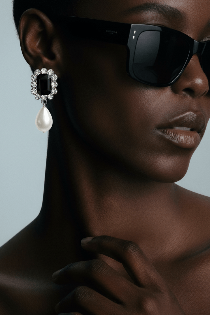 Close-up of a woman wearing  black gemstone center statement drop pearl earrings and black sunglasses with a blurred background