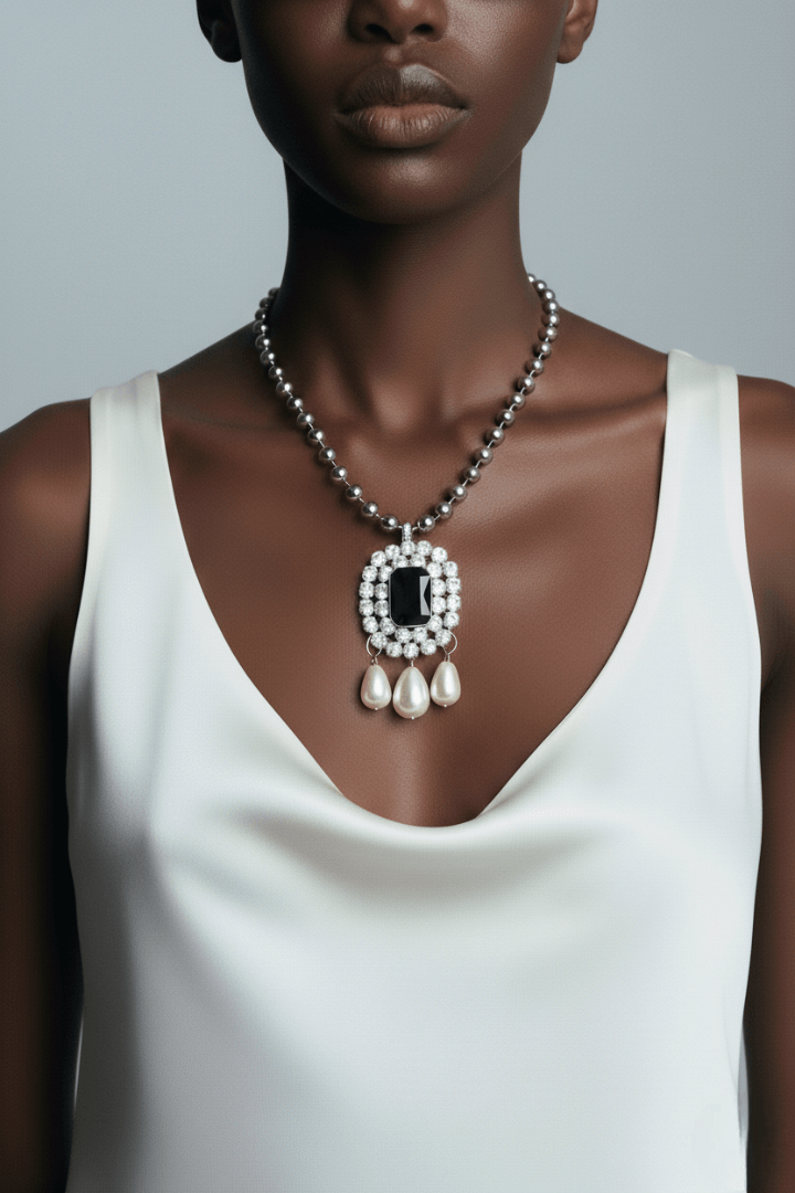 Woman wearing a Pearl necklace with a black gemstone and pearl drops with a white top against a gray background