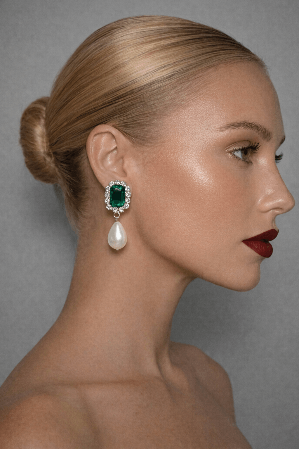 Woman wearing a green emerald and pearl earring against a gray background