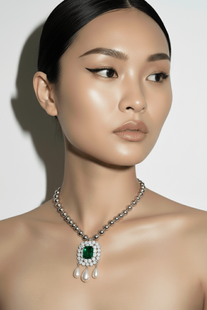 Woman wearing a necklace with an emerald pendant and teardrop pearls on a plain background