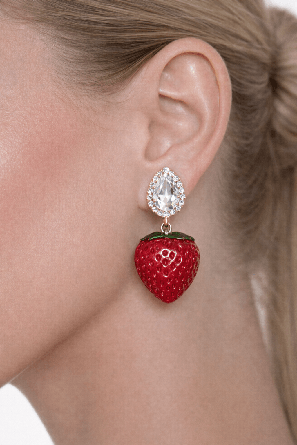 Red strawberry-shaped earring with a teardrop-shaped gemstone worn by a person.