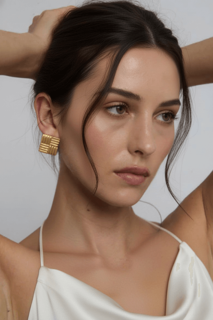 Woman wearing vintage-inspired gold geometric earrings with a neutral background