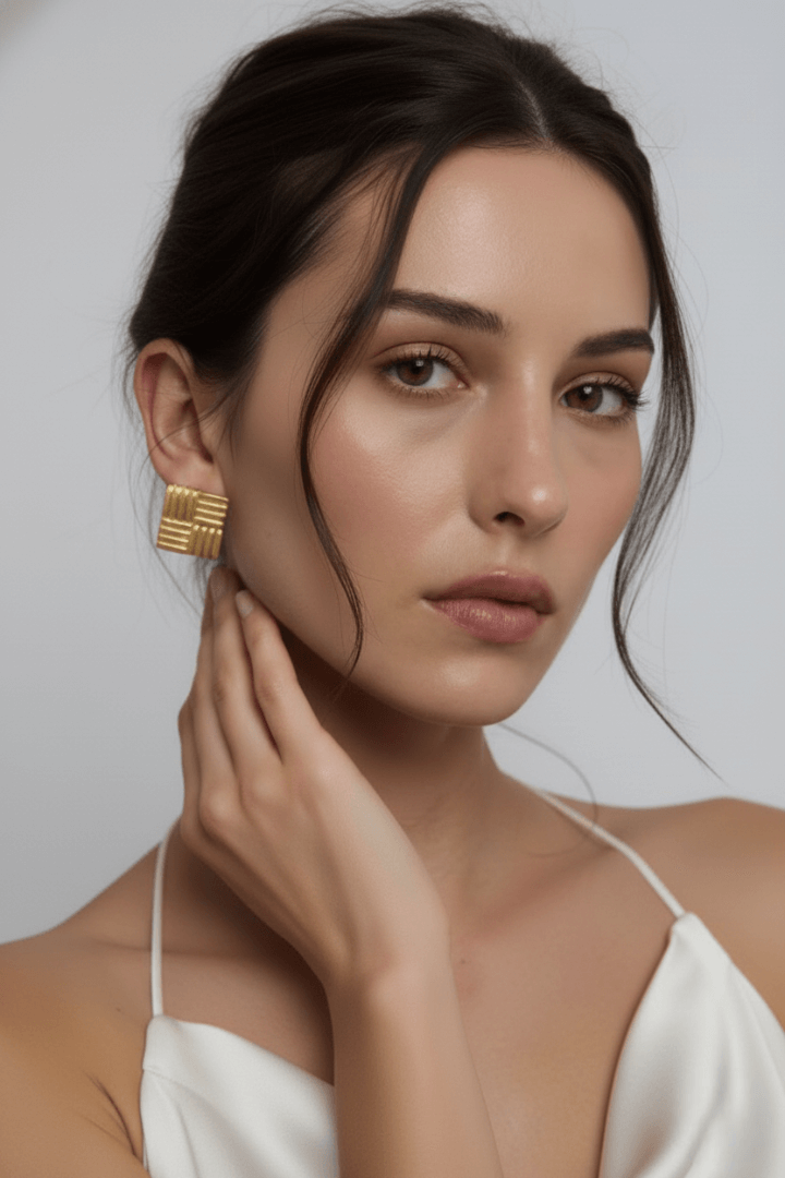 Woman wearing Vintaras gold square earrings and a white top against a neutral background