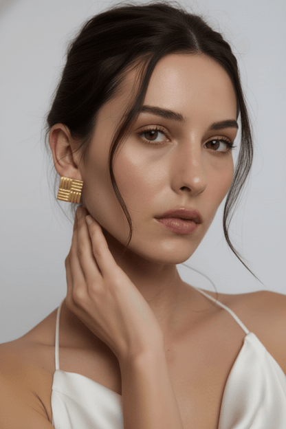 Woman wearing Vintaras gold square earrings and a white top against a neutral background
