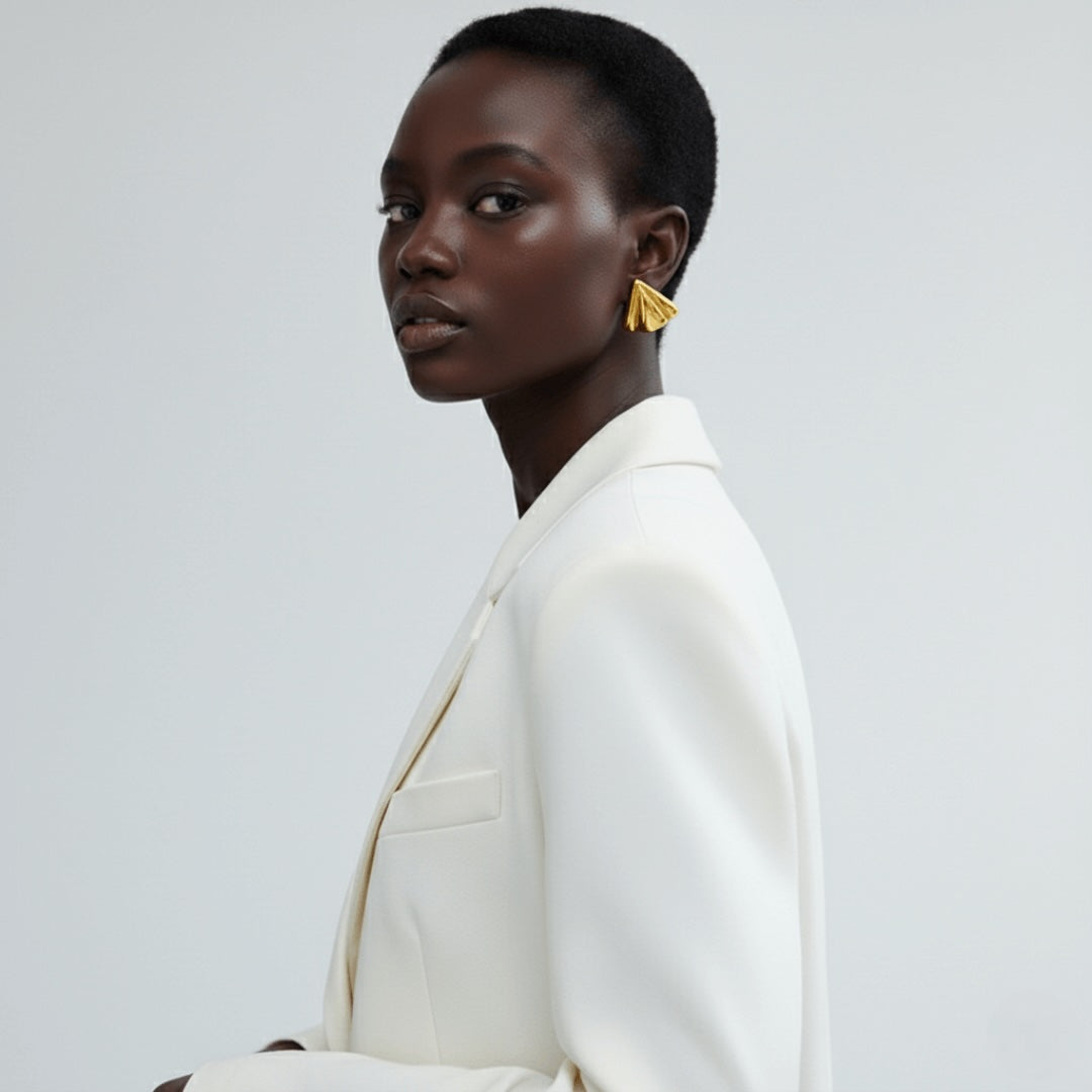 Model wearing Vintaras Solis Earring Gold and a white blazer on a light gray background