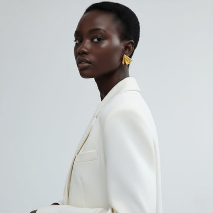 Model wearing Vintaras Solis Earring Gold and a white blazer on a light gray background