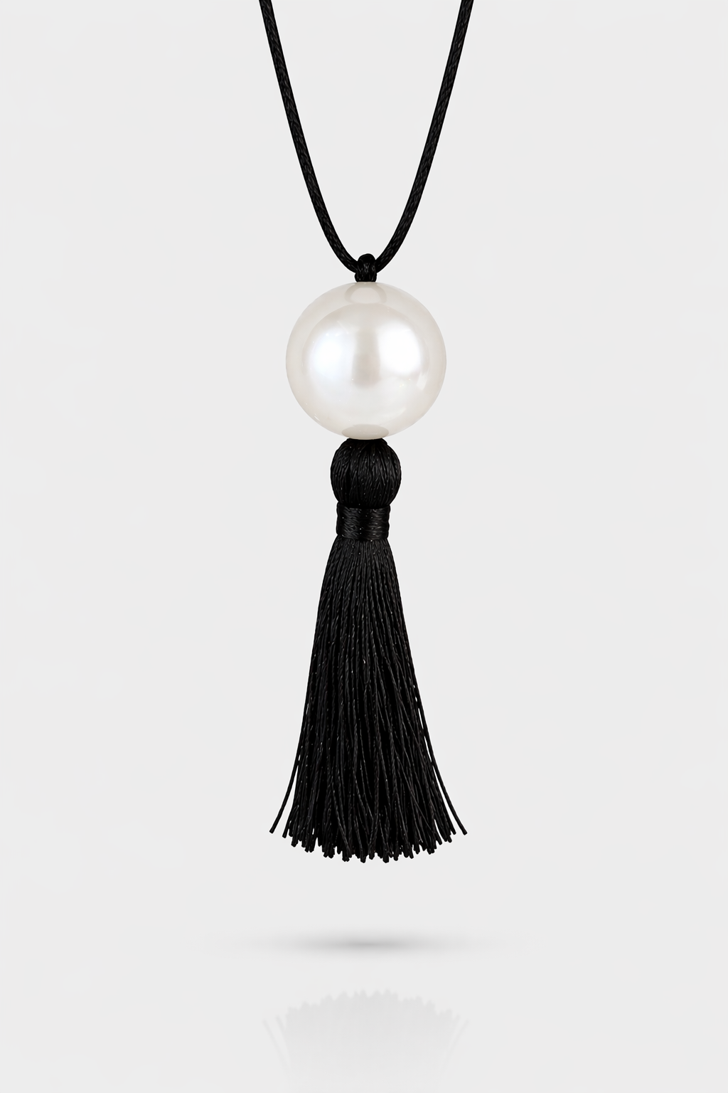 Necklace with a large pearl pendant and black tassel on a white background