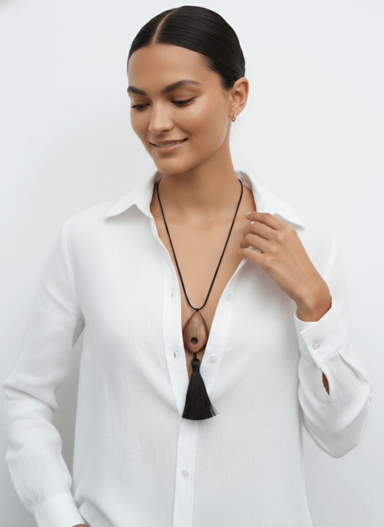 Woman wearing a white shirt with an open collar, revealing a black necklace with tassels, Vintaras Bette Tassel Necklace .