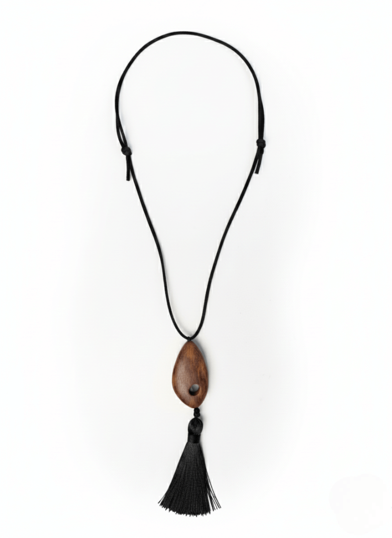 Vintaras Bette Tassel Necklace, a necklace with a wooden pendant and black tassel on a white background.