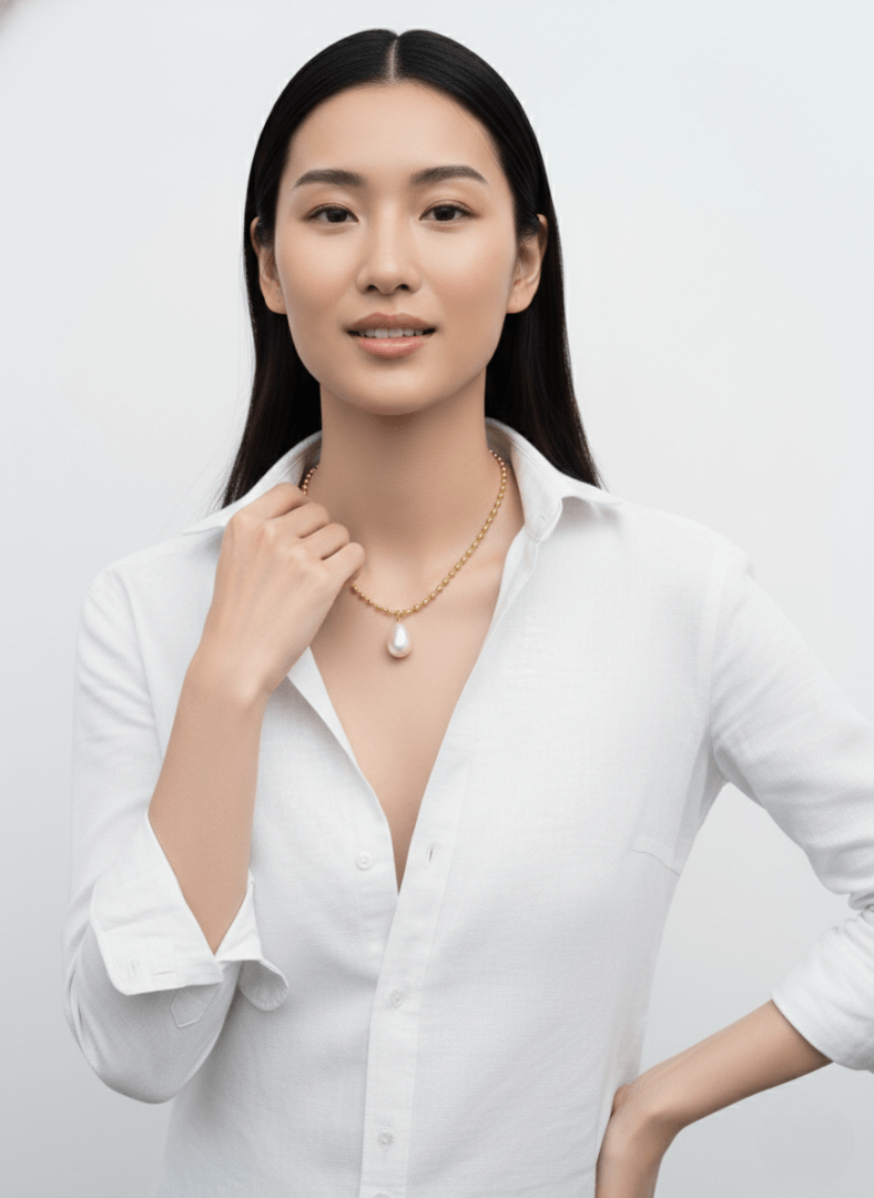 Woman wearing a tear drop pearl pendant necklace, Vintaras Ingrid Necklace Gold , against a plain background